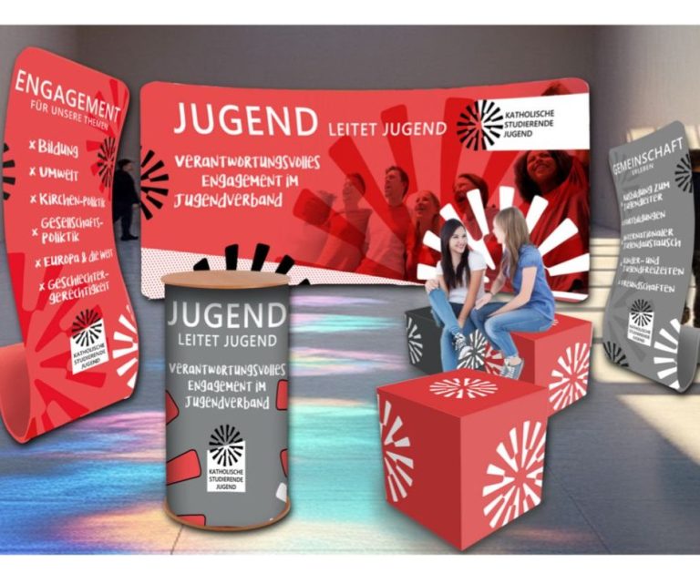 Das Bild zeigt eine Messeausstattung mit Hintergrundwand, Seitenaufstellern und Sitzwürfel